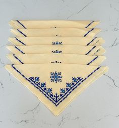 six blue and white handkerchiefs on a marble countertop, each with an embroidered design