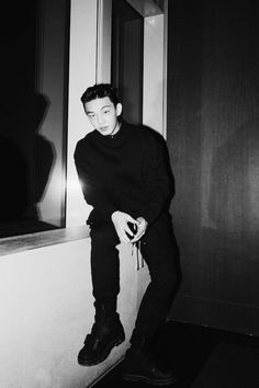 black and white photograph of a young man sitting on a ledge looking at the camera