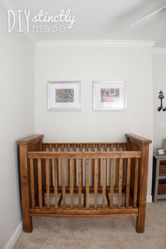 a wooden crib sitting in the corner of a room next to two framed pictures