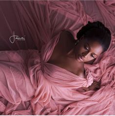 a woman laying in bed covered with pink sheets