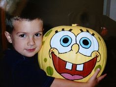 a young boy holding up a spongebob pumpkin with his face painted on it