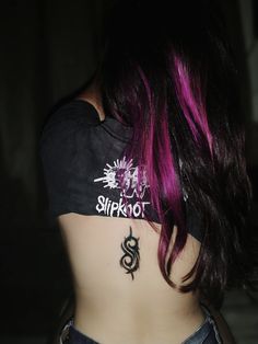 the back of a woman with pink hair and tattoos on her upper half, wearing jeans