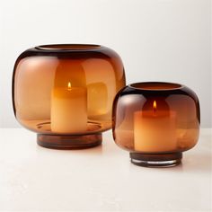 two brown glass vases sitting next to each other on a white counter top with one candle in the middle