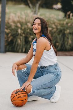 a woman sitting on the ground with a basketball in her hand and smiling at the camera