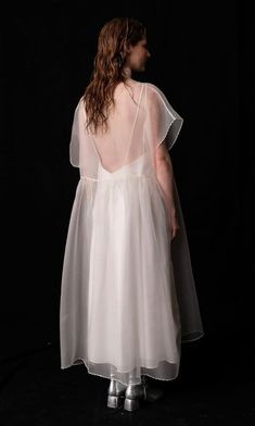 a woman in a white dress is standing against a black background with her back to the camera