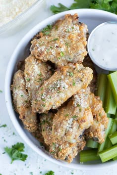 a white bowl filled with chicken wings, celery and ranch dressing next to rice