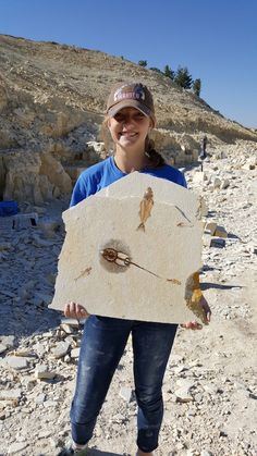 a woman holding up a plaque with two birds on it in front of some rocks