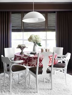 a dining room table with chairs and a vase on top of it in front of a window