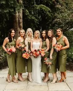 a group of women standing next to each other in front of trees and flowers on the ground