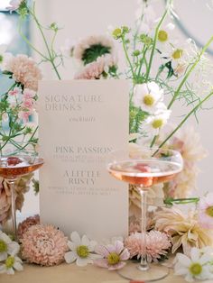 a table topped with two wine glasses filled with pink and white flowers next to a menu