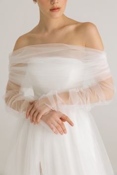 a woman wearing a white dress with sheer tulle on the shoulders and arms, in front of a white background