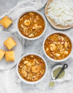 three bowls filled with shrimp and rice on top of a white cloth next to two plates