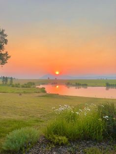 the sun is setting over a lake and grassy field