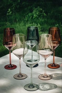 several wine glasses are lined up on a table outside in front of some grass and trees