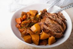 a white bowl filled with meat and vegetables on top of a table next to a napkin