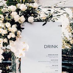 a drink menu sitting on top of a table next to white flowers and greenery