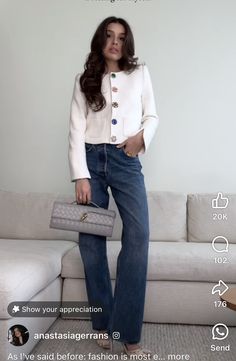 a woman standing next to a couch holding a purse