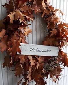 a wreath with leaves and a sign that says herbszuber on it hanging from the side of a door