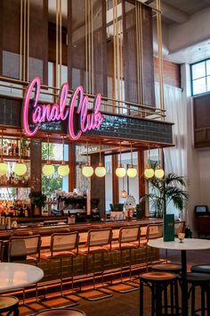 the inside of a restaurant with tables, chairs and neon signs on the wall above it