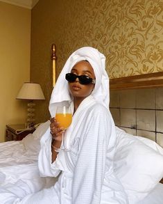 a woman sitting on a bed holding a glass of orange juice