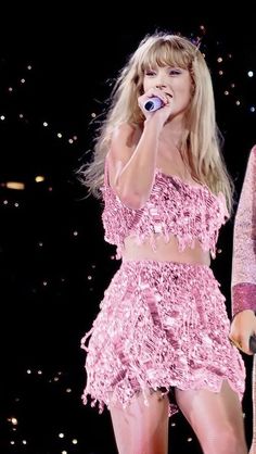 two women are performing on stage with microphones in their hands and one is wearing a pink outfit