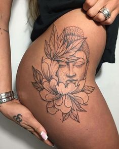 a woman's thigh with a buddha tattoo on it and flowers around the thighs