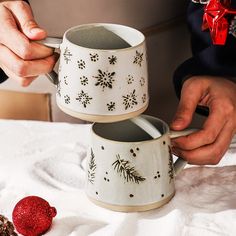 two mugs with designs on them being held by someone's hands over a table