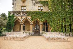 an outdoor wedding venue with white chairs and greenery on the side of the building