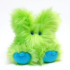 a green stuffed animal with blue eyes and fur on it's legs, sitting in front of a white background