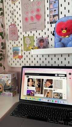 an open laptop computer sitting on top of a desk next to a wall covered in pictures