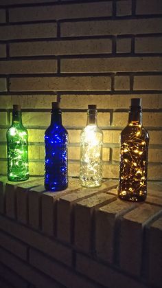 three different colored bottles sitting on top of a brick wall with lights in the bottom