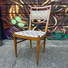 a wooden chair sitting in front of a wall with graffiti on it's side