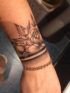 a woman's arm with a flower tattoo on it and a gold chain around the wrist