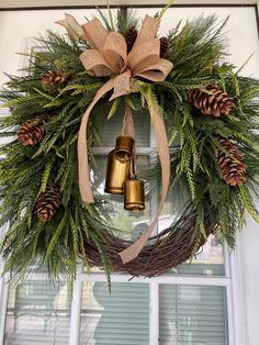 a wreath with two bells hanging from it and pine cones on the window sill