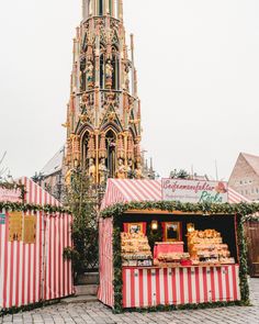 an outdoor food stand with red and white striped tents in front of a tall building