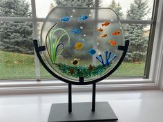 a glass fish bowl sitting on top of a metal stand in front of a window