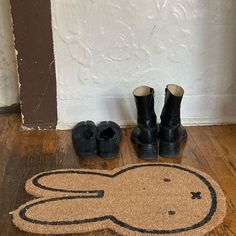 a pair of black boots sitting on top of a wooden floor next to a door mat