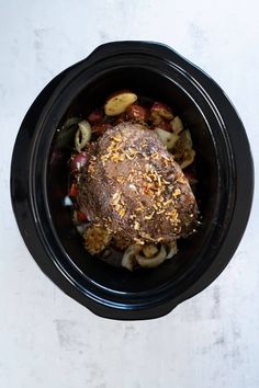 a black slow cooker filled with meat and vegetables on top of a white table