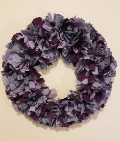 a wreath made out of purple and grey paper on a white wall with the letter o in the center