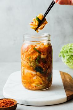 a person holding chopsticks above a jar filled with food on top of a cutting board