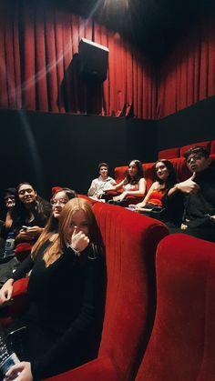 a group of people sitting in red chairs next to each other watching something on the screen