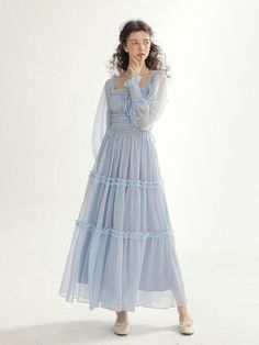 This product is an Isabel Smock Long Dress that exudes romantic elegance with its tiered tulle skirt and delicate smocking detail. The long sleeves are complemented by the smocked bodice, offering a snug fit with a vintage flair. This dress combines the airy lightness of the fabric with the intricate detail of the smocking, creating a harmonious blend of sophistication and whimsy. - The dress is adorned with tiered tulle layers, each accented with a ruffle trim, adding dimension and a fairy-tale quality.- Its smocked bodice provides both comfort and a tailored appearance, enhancing the dress's feminine appeal.- The long, sheer sleeves offer coverage while maintaining the dress's ethereal aesthetic.- Crafted for those special occasions, the Isabel Smock Long Dress is a beautiful choice Light Blue Cottagecore Dress, Ethereal Dress Casual, Elegant Long Sleeve Smocked Dress With Smocked Cuffs, Elegant Long Sleeve Smocked Dress, Feminine Smocked Dress With Long Sleeves, Elegant Smocked Dress With Ruffles And Tiered Skirt, Fitted Smocked Long Sleeve Dress With Ruffles, Feminine Smocked Dress With Ruffles And Long Sleeves, Feminine Long Sleeve Smocked Dress With Ruffles