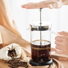 a person is pouring coffee into a french press on top of a table with beans