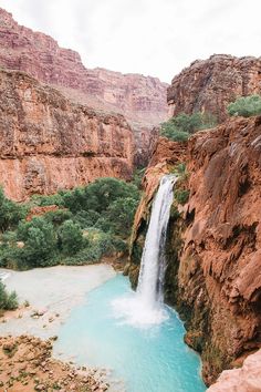 a waterfall in the middle of a canyon with blue water and green trees around it