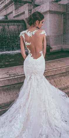 a woman in a wedding dress standing near a fountain with her back to the camera