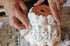 two hands are working on an object made out of seashells and other items