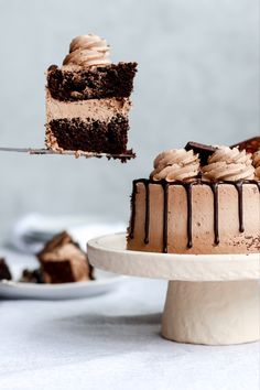 a piece of chocolate cake being lifted by a fork with the rest of the cake in the background