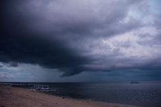 boats on the water under a cloudy sky at the beach in front of an ocean