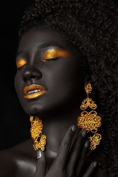 a woman with gold makeup and jewelry on her face, holding her hands to her chest