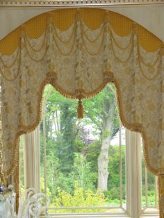 an ornate window with curtains and valances in the center, overlooking a lush green park